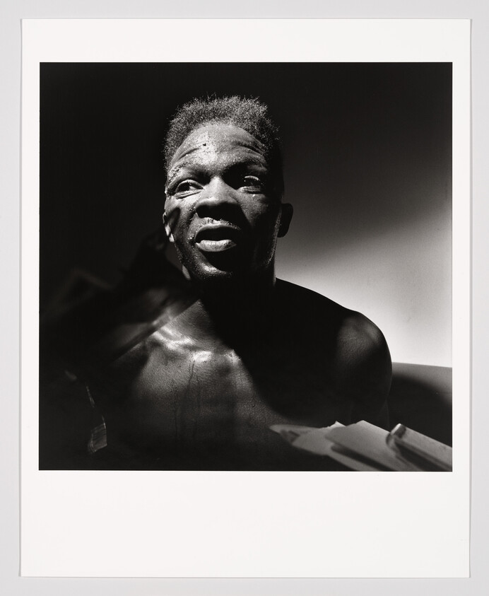 Man with glistening skin looks upward in dramatic high-contrast lighting.