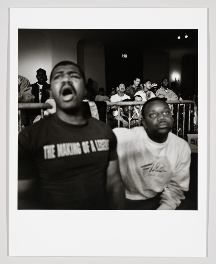 Two men in the front row react passionately, one shouting while a crowd watches behind them.
