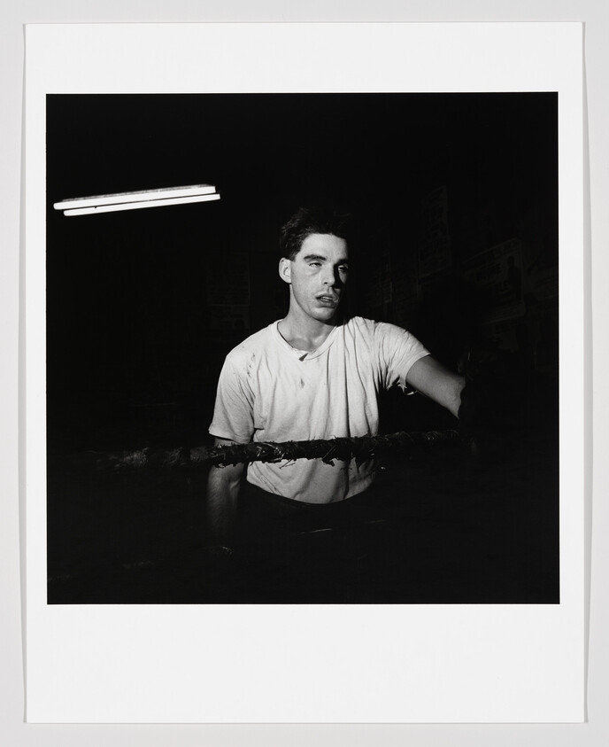 A tired young boxer leans on the ring ropes under a single fluorescent light.
