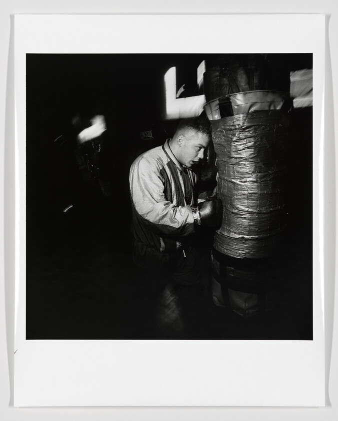A young man wearing boxing gloves practices punches on a heavily taped punching bag.