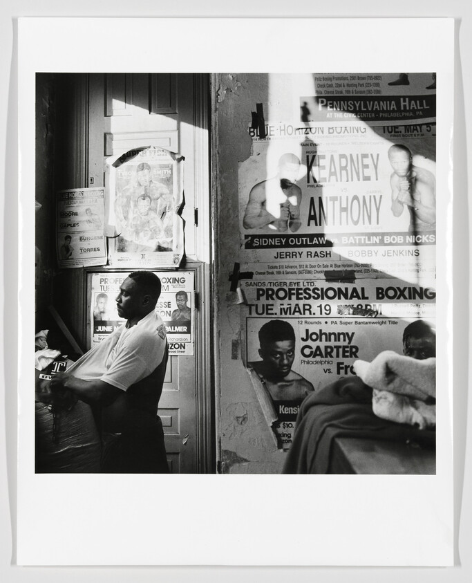 A man stands leaning against a wall covered in vintage boxing posters.