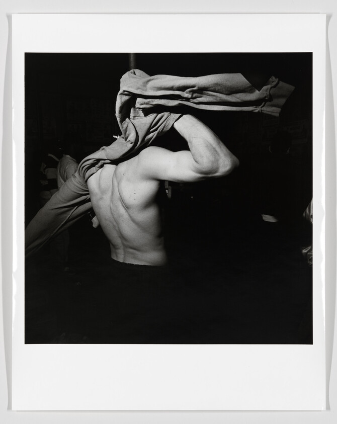 Shirtless man pulling a sweatshirt over his head, highlighting his muscular back.