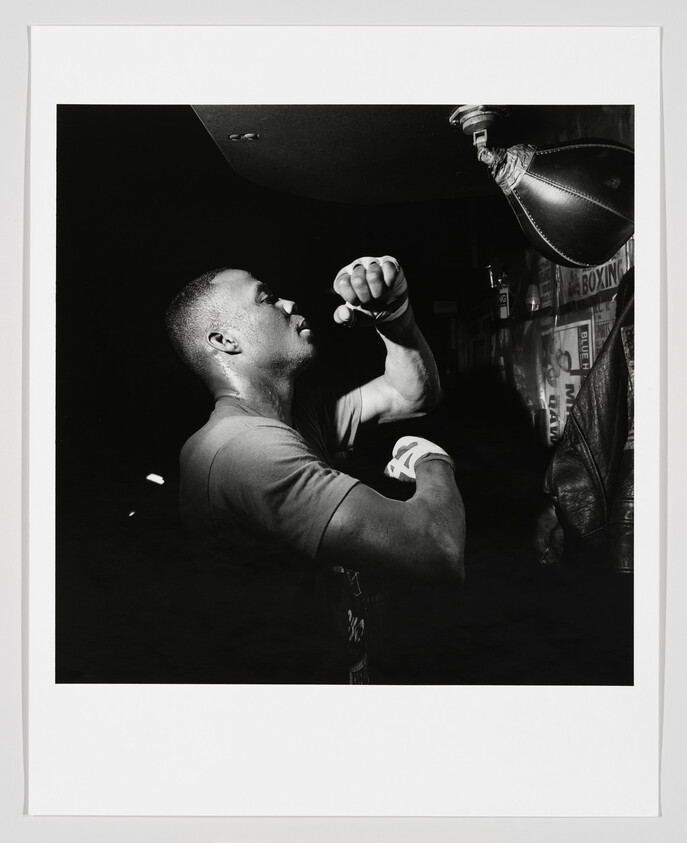 A boxer with wrapped hands punches a hanging speed bag in a dim gym.