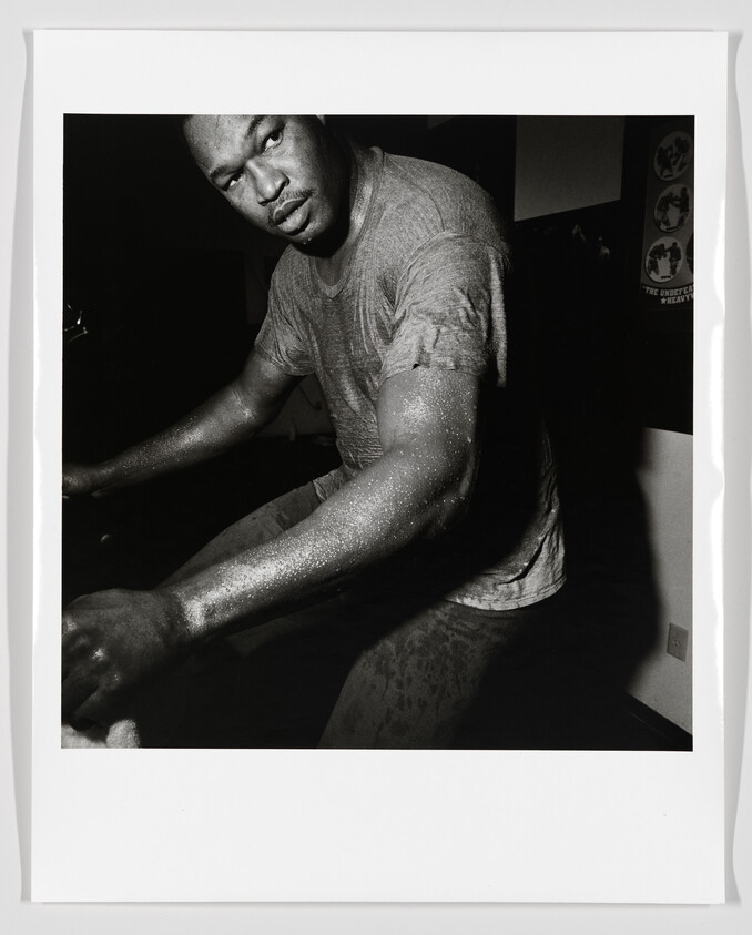 A sweaty man leans forward intensely while pedaling an exercise bike in a dim room.