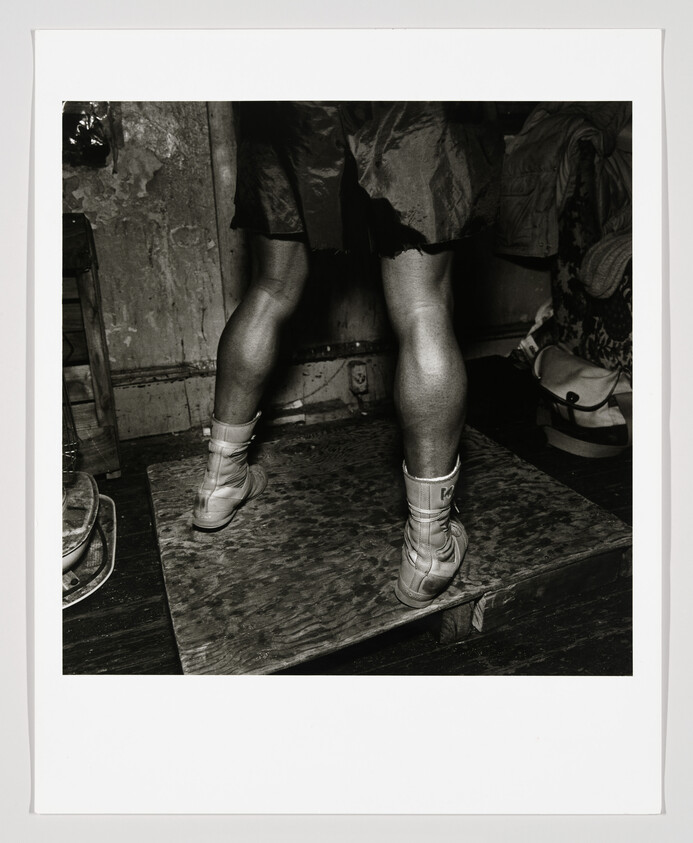 A person standing on a worn wooden platform wearing lace-up boots and a torn skirt.