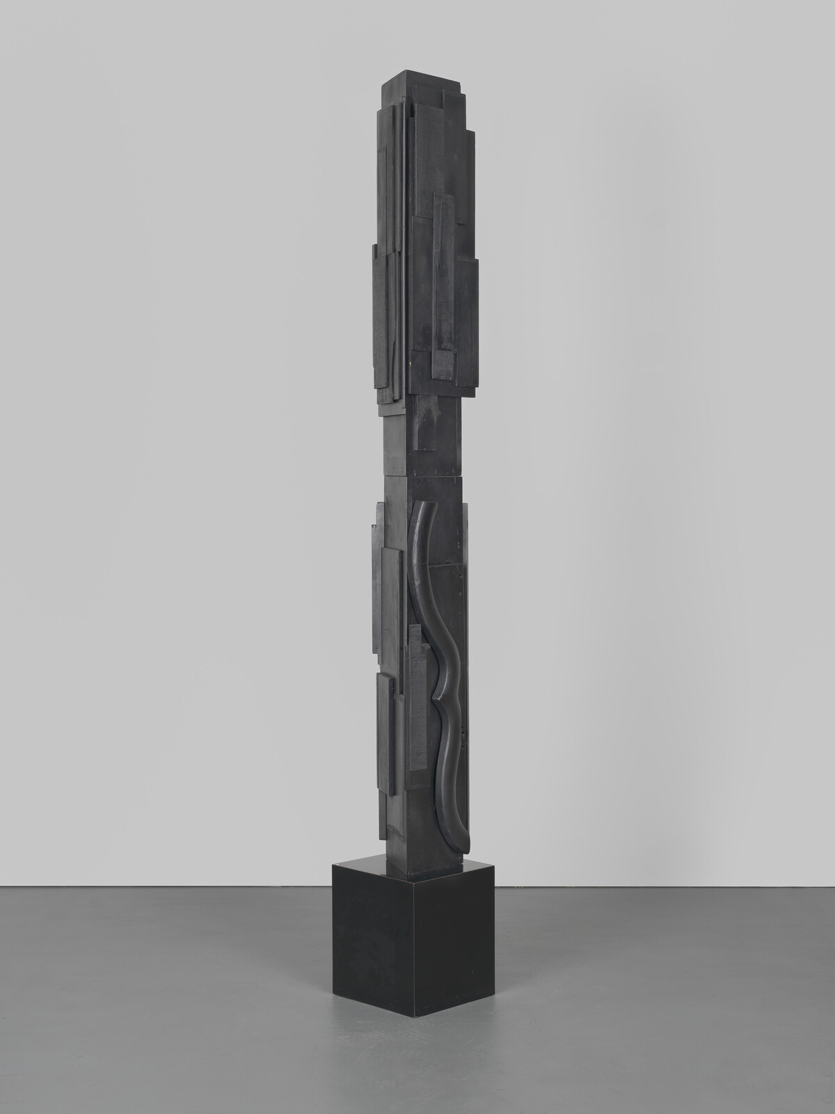 Tall, abstract black sculpture with geometric shapes and curves, standing on a square base.