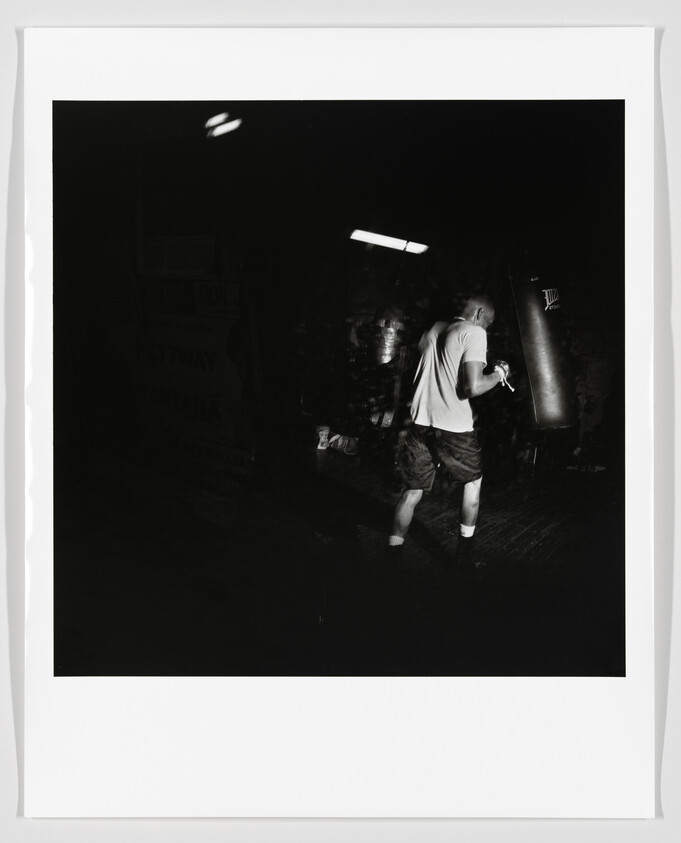 A man practices boxing with a punching bag in a dimly lit gym.