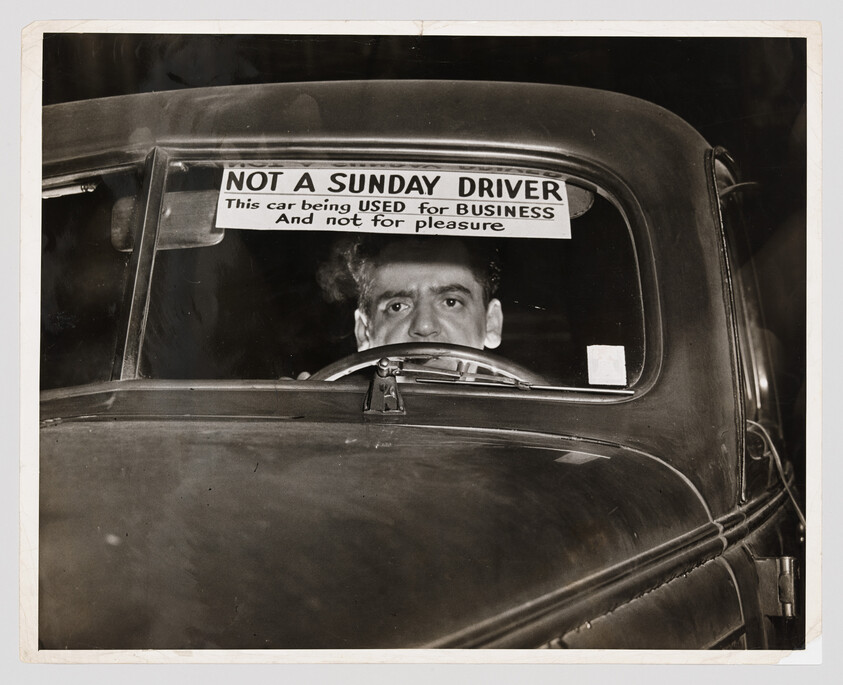 Man sits behind steering wheel of car with sign saying "Not a Sunday driver" indicating business use.