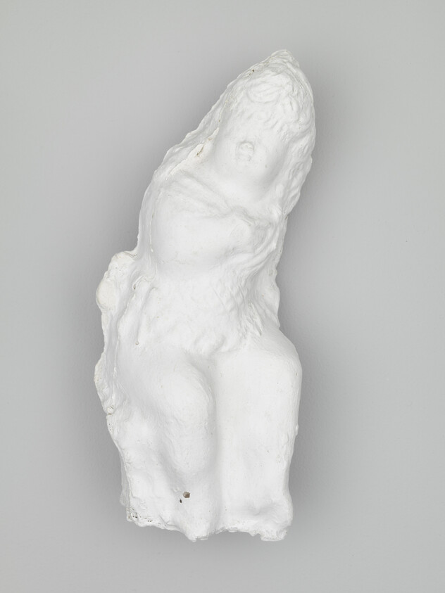 Abstract white plaster sculpture resembling a seated figure with rounded, worn features.