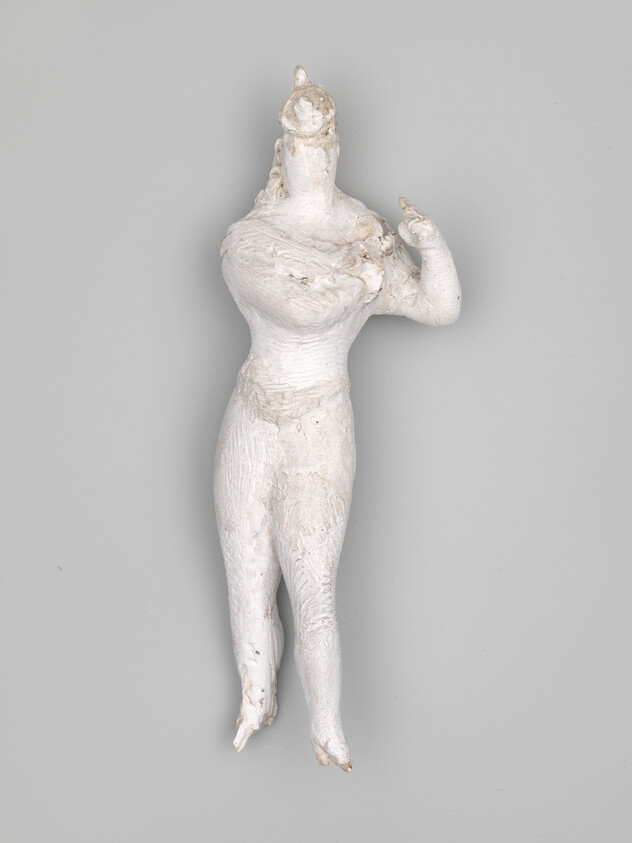 Small white plaster figure of a standing human with one arm raised and crossed torso.