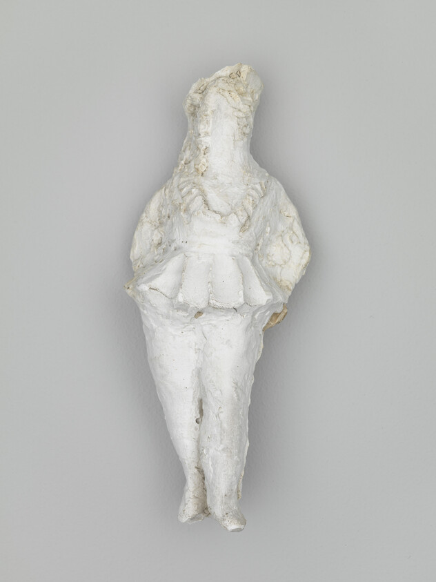A small white plaster figurine of a standing person wearing a short skirt.