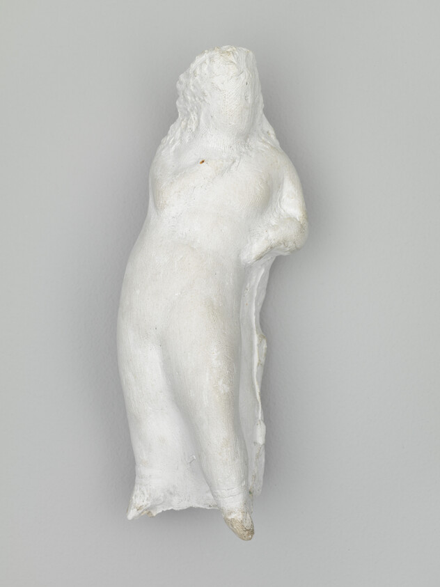 Small white plaster sculpture of a leaning female torso missing head and arms.