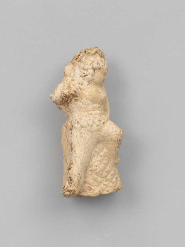 Small worn terracotta figurine of a seated child with one leg raised.