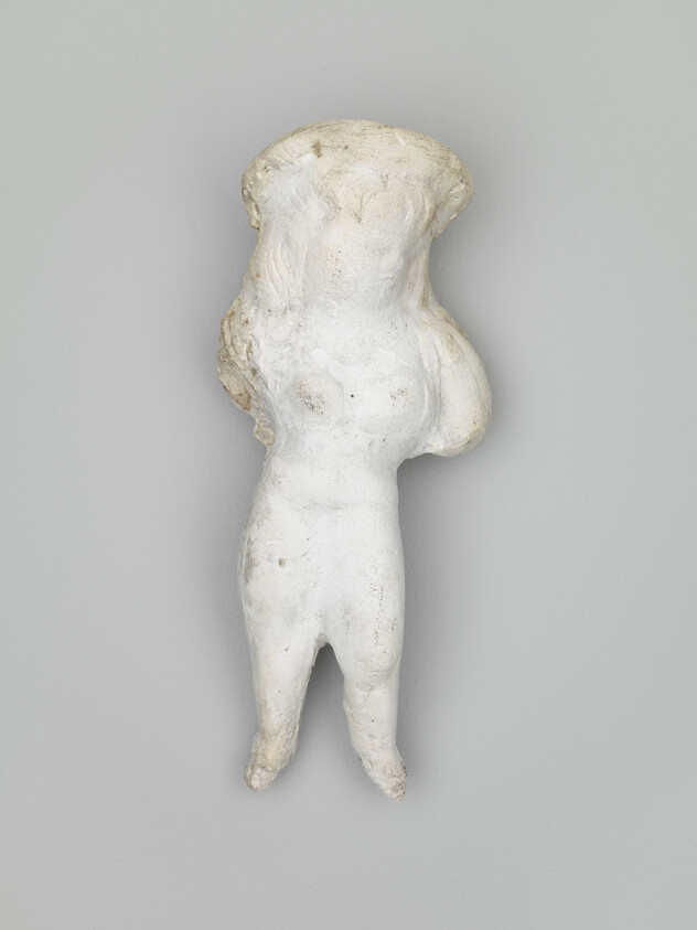 Small worn white clay figurine of a standing female with missing arms and head.