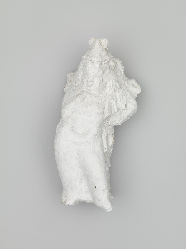 A rough white plaster sculpture of a female torso mounted on a gray wall.