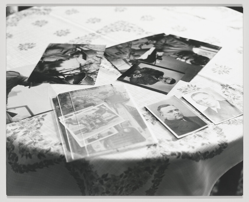 A collection of black and white photographs spread out on a patterned tablecloth, capturing various people and moments from the past.