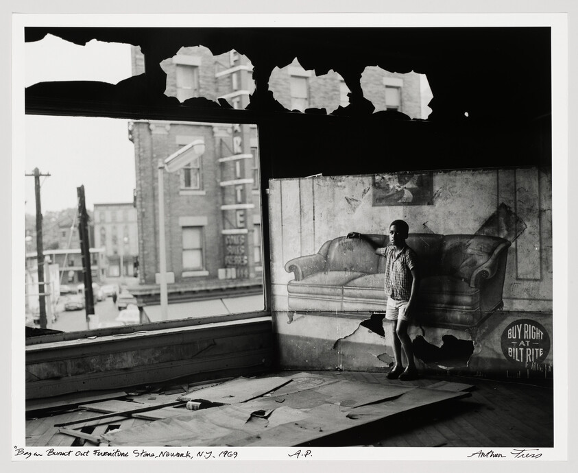 Young boy stands leaning on a painted couch in a dilapidated room with torn ceiling.