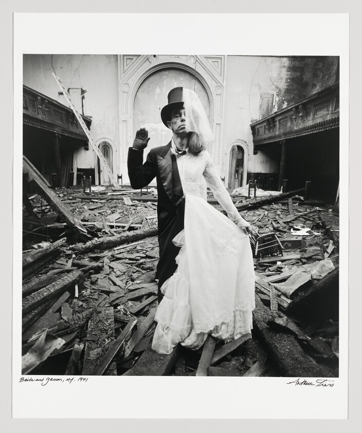A bride and groom stand in wedding attire amid a ruined, debris-filled church interior.
