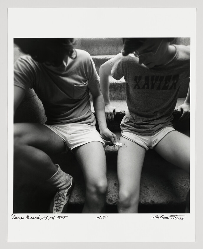 Two teenagers sit on concrete steps while one applies a small bandage to the other's thigh.