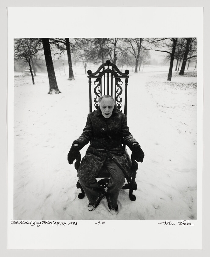 Elderly man in a winter coat sits on an ornate high-backed chair in a snowy park.