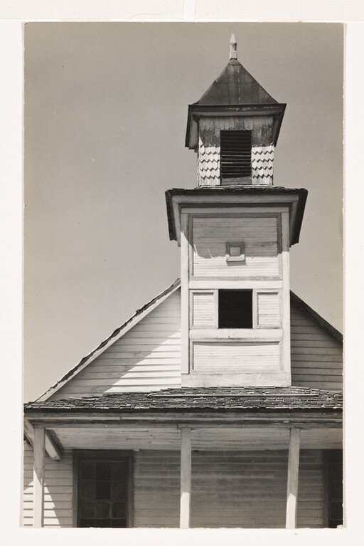 Abandoned wooden bell tower rising above a weathered gable roof and porch.