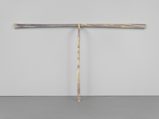 A T-shaped painted wooden beam leans against a white gallery wall, mottled yellow and purple.