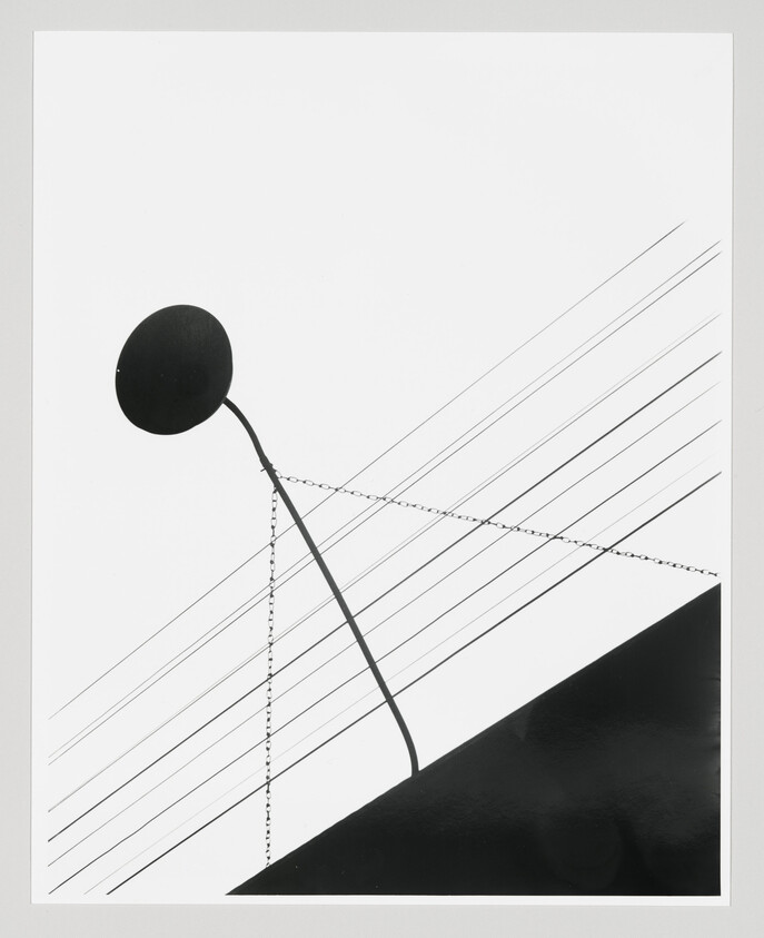 A leaning round sign on a curved pole held by chains above angled power lines and a dark slope.