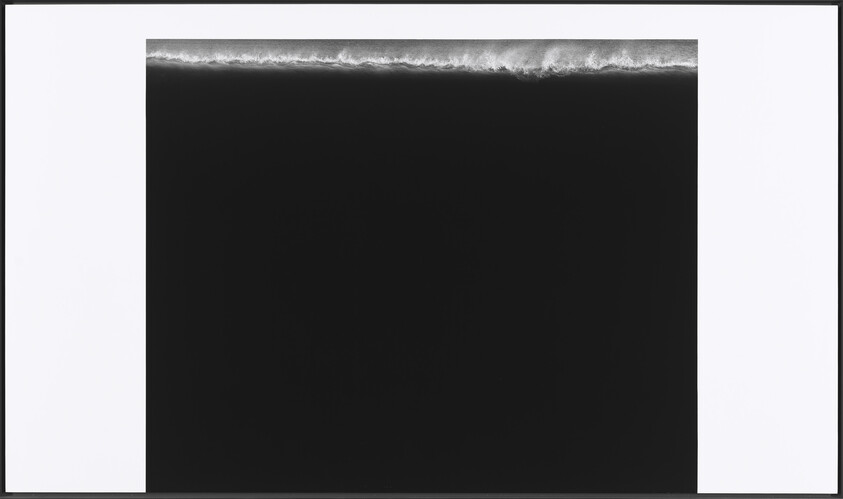 Aerial view of a dark ocean with a thin line of breaking white waves along the top edge.