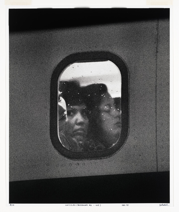 Two passengers’ faces pressed against a rain-speckled train window, seen in black and white.