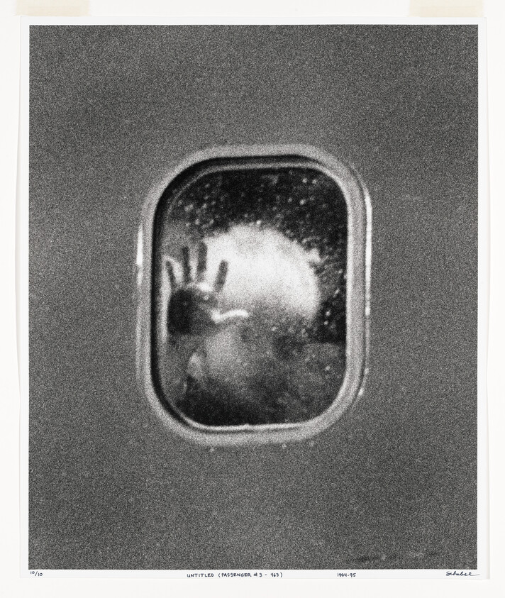 A silhouetted passenger presses a hand against a small airplane window during flight.