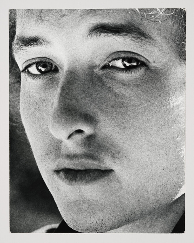 Close-up black and white portrait of a young man with a neutral expression, focusing on his eyes and the details of his face.