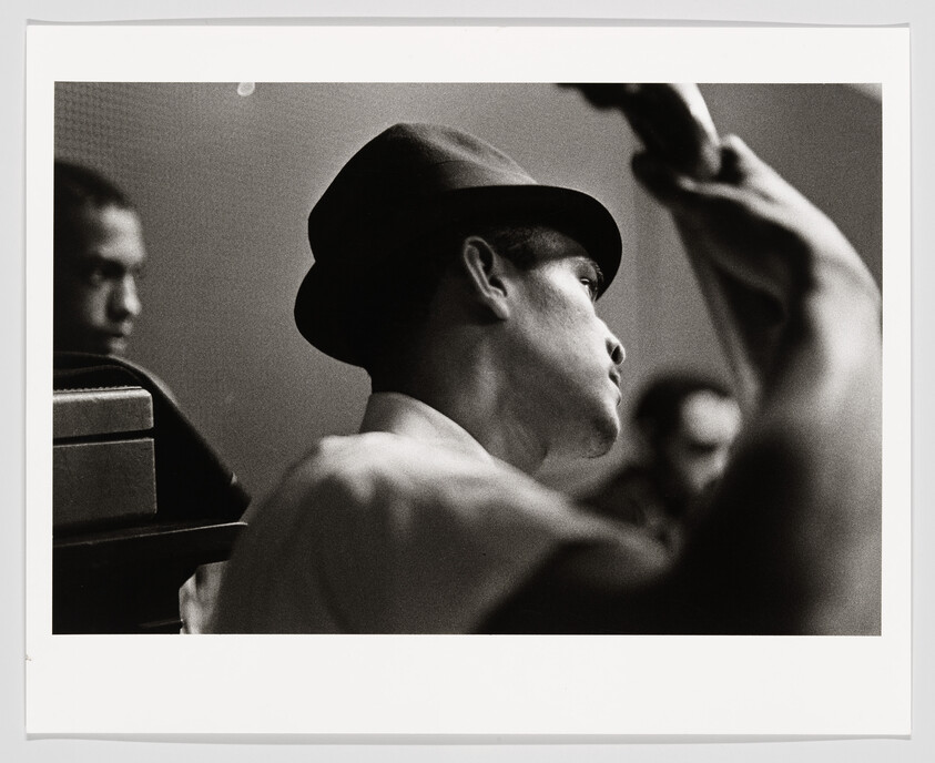 Man wearing a hat plays upright bass with raised arm while two musicians watch.