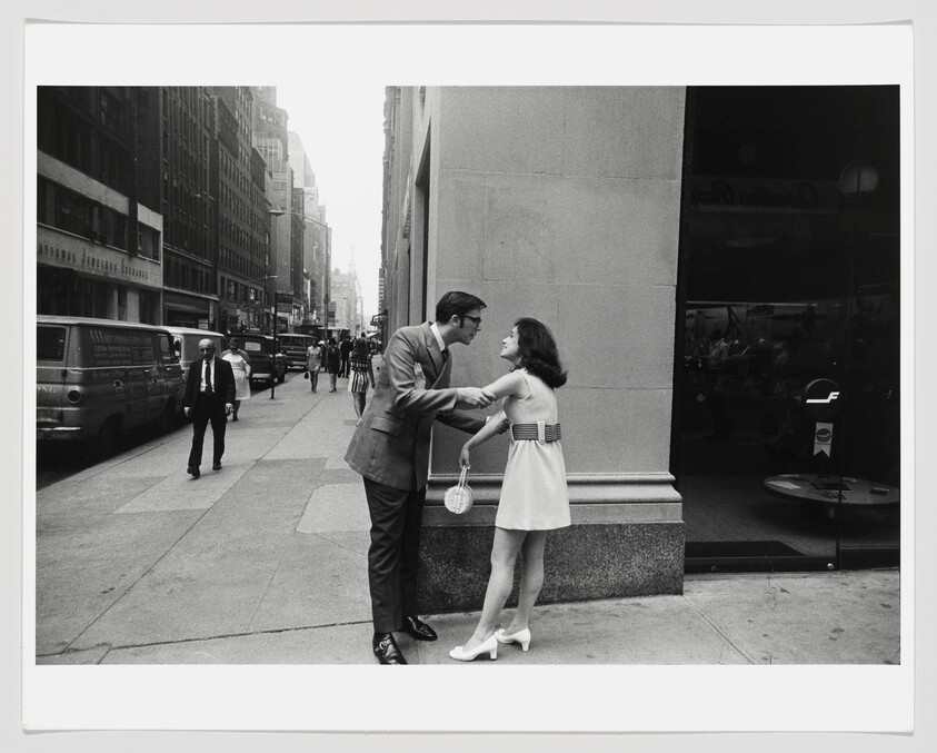 A man holds a young woman's arms as they talk on a busy city sidewalk.