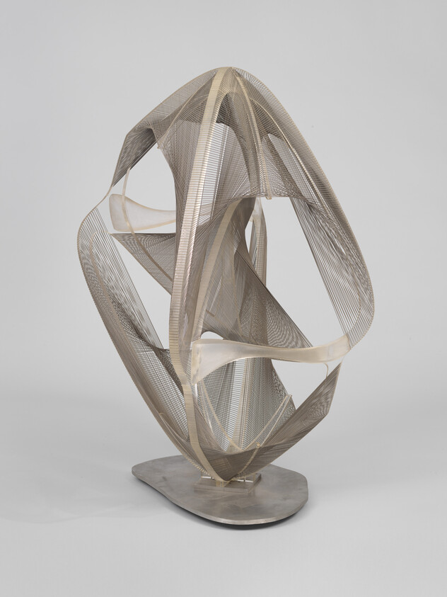 A looping ribbon-like metal mesh sculpture with twisting forms mounted on a flat base.