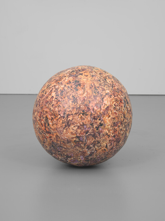 A large marbled brown-orange sphere sits centered on a gray gallery floor against a light wall.