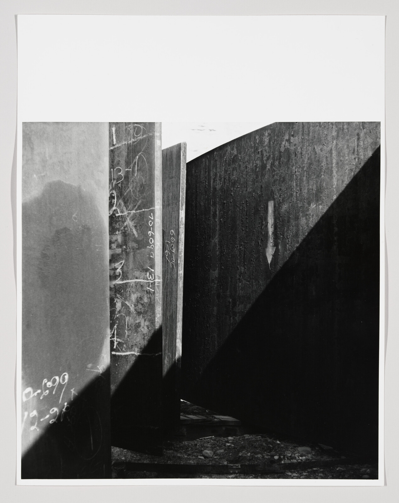 Tall concrete walls with chalk markings and a sharp diagonal shadow creating a narrow passage.