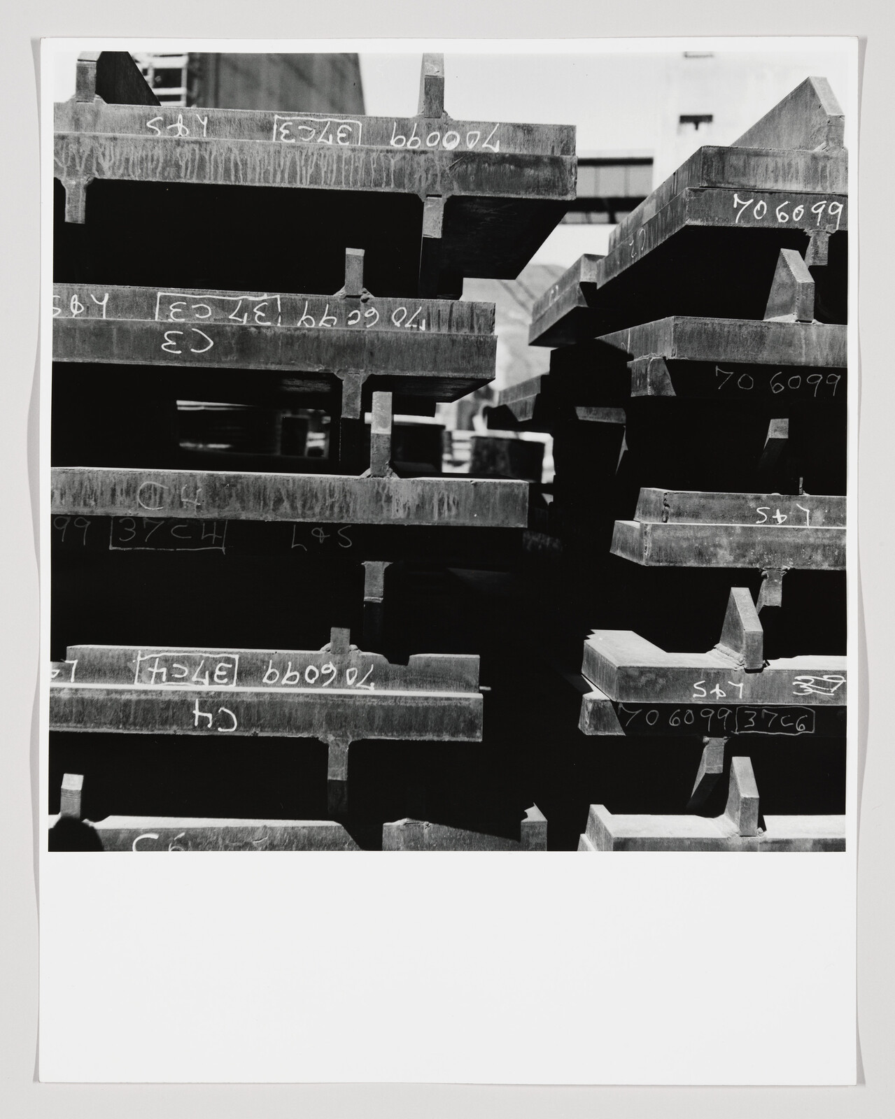 Stacked steel I-beams with chalk markings stored in a warehouse, arranged in horizontal rows.