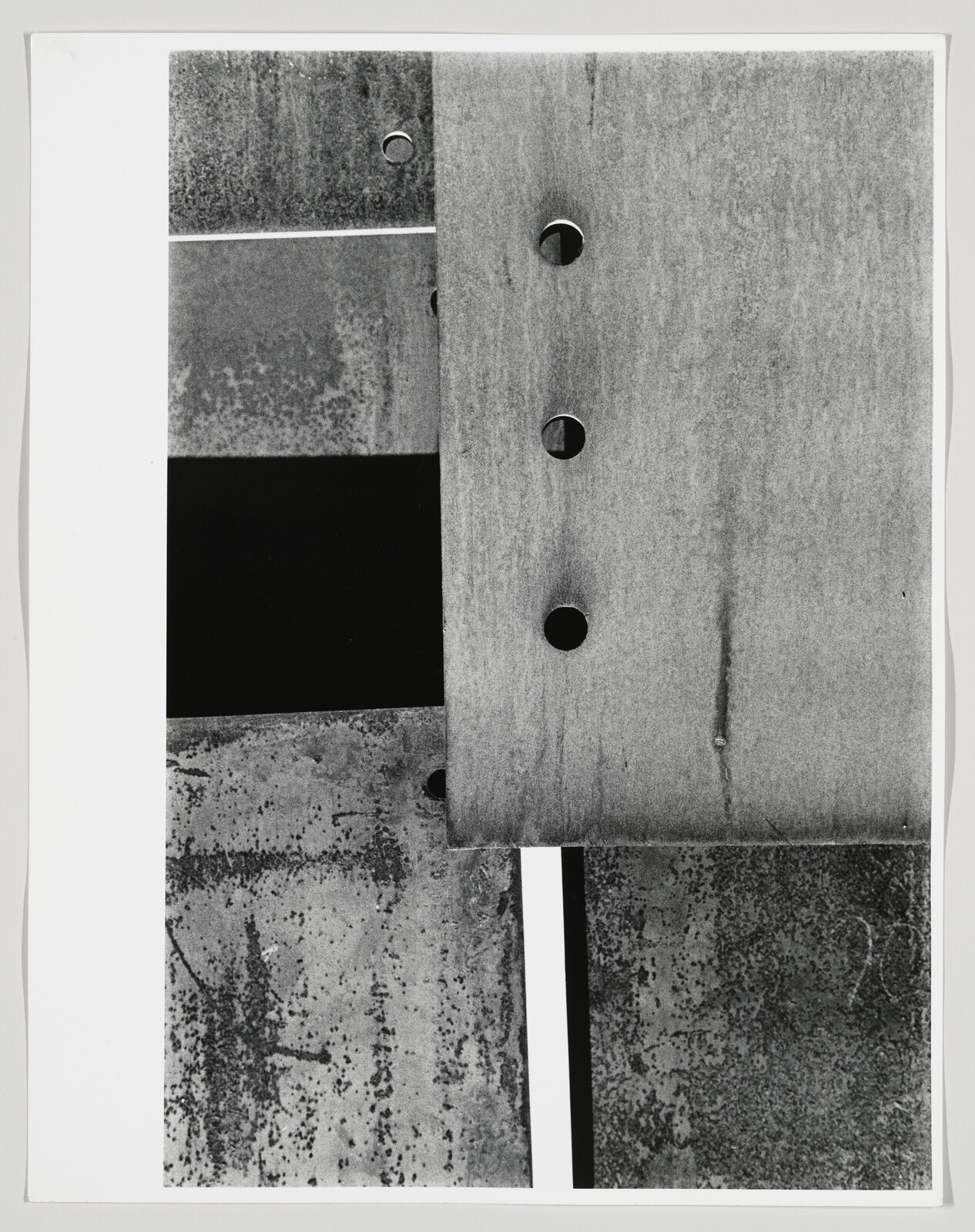 Overlapping weathered metal plates with circular holes create a high-contrast abstract composition.