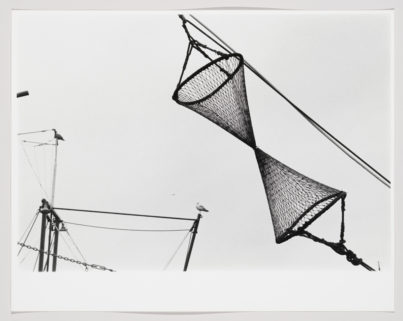Two conical fishing nets hang from boat rigging while a seagull perches on a mast.