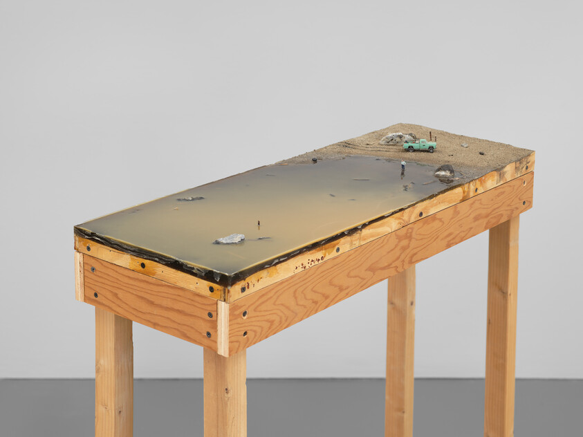 A wooden pedestal holds a shallow resin landscape with a tiny green truck and small figures.