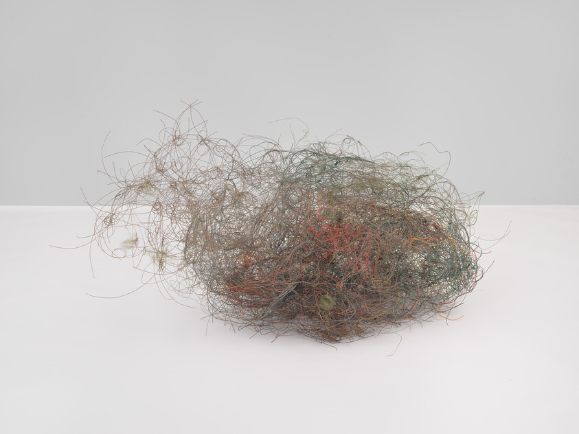 A tangled ball of fine multicolored wires and threads resting on a white surface.