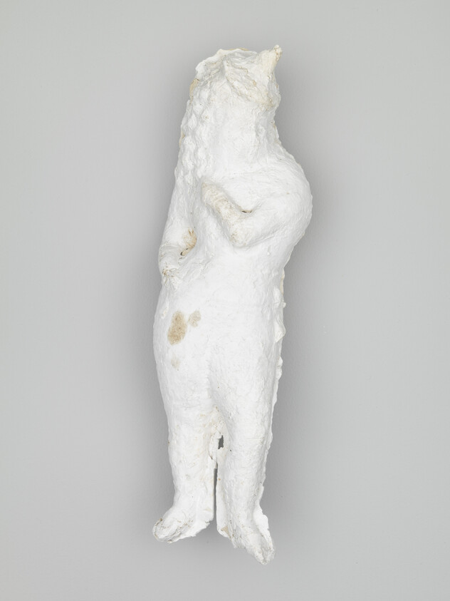 A rough white plaster sculpture of a standing human figure with hands near the chest.