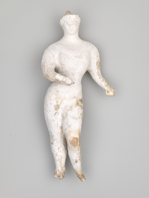 Worn white terracotta figurine of a standing female with partially damaged arms and surface.