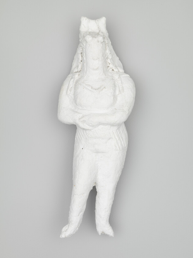 Plaster sculpture of a standing person with crossed arms and long hair or headdress.