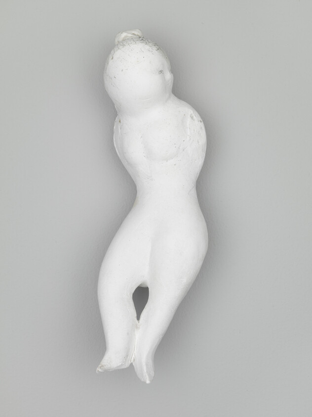 A small white plaster sculpture of an abstract seated human figure with fused legs.