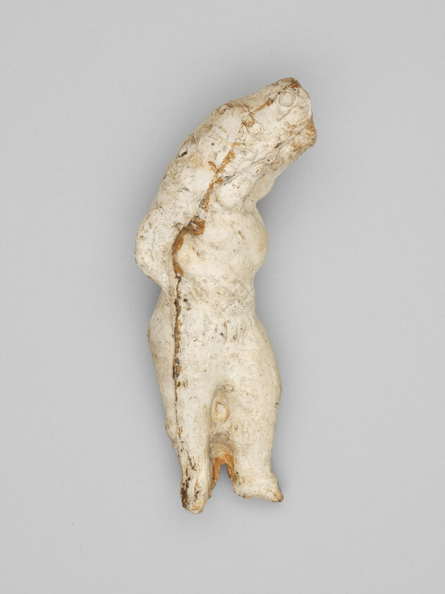 Worn white plaster figurine of a standing nude torso missing head, arms, and lower legs.