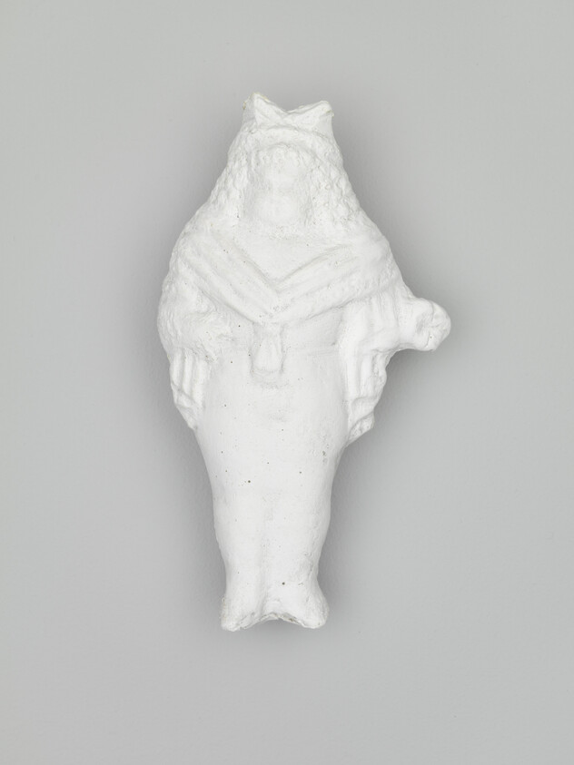 Small white plaster figurine of a seated woman with folded arms against a gray background.