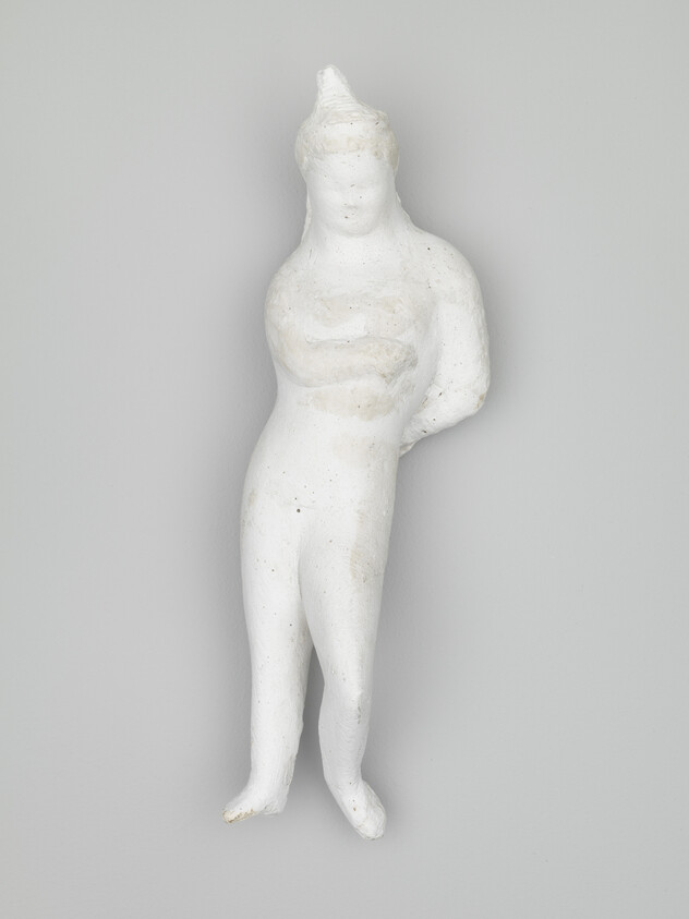 Small white clay figurine of a standing human with arms behind its back.