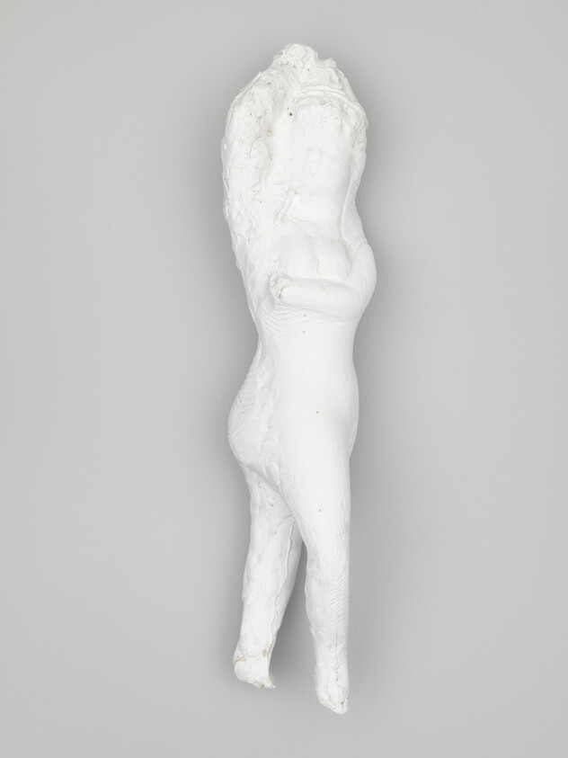 A white plaster sculpture of a standing human figure with crossed arms and long textured hair.