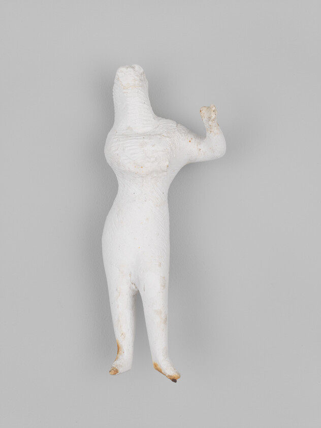 Headless white clay figurine of a female body with one raised arm and small legs.
